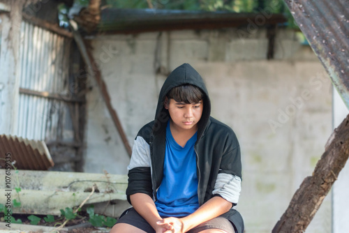 Asian teenage boy in a black t-shirt and coat stood and sat in a secret place with a sad expression suppressed due to friendship problems, family problems, and drug problems, soft focus.