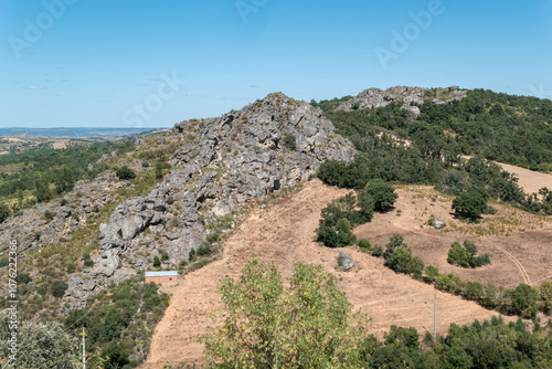 Paisagem montanhosa com grandes formações rochosas, em meio a um campo rural, sob um céu azul photo