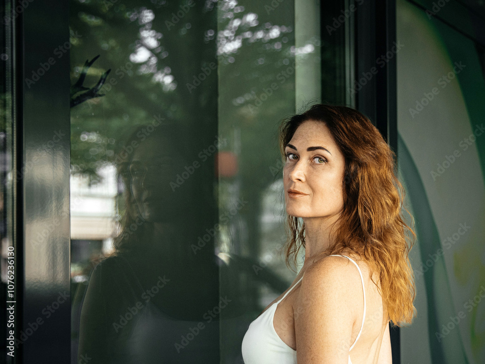 Woman with expression looking over shoulder near reflective glass wall Woman with expression looking over shoulder near reflective glass wall