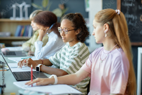 Side view of diverse group of children sitting in row in school classroom and using computer