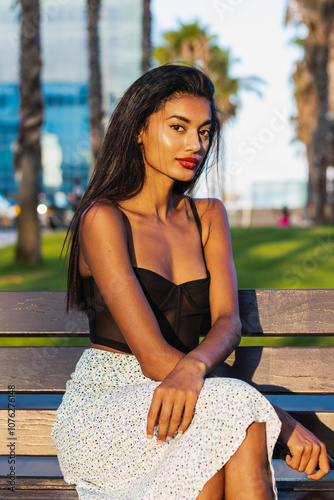 Beautiful young indian woman sitting on a park bench in a modern city