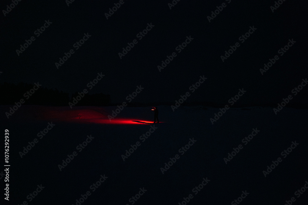 A Person in the Snow Shining a Red Flashlight in the Dark
