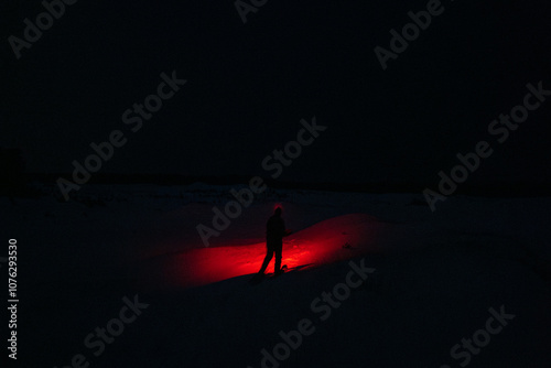 Obraz na płótnie A Person in the Snow Shining a Creepy Red Flashlight in the Dark Night w salonie