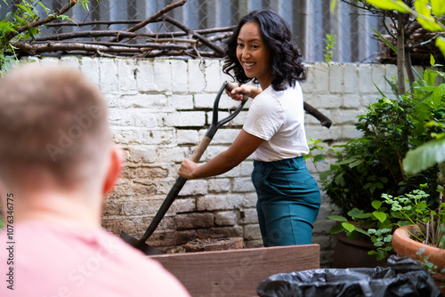 Smiling woman using shovel and talking to friend in urban garden photo