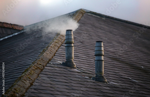 A frontal view of two galvanised metal chimney exhausts on a sloping slate roof