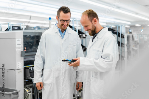 Technicians in white lab cots disussing over electronic component photo