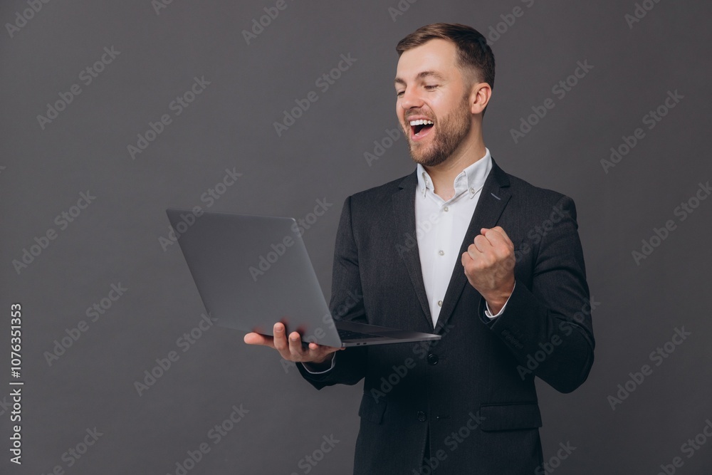 Portrait of confident businessman in gray suit showing yes with hand, successful deal, working with laptop while standing over gray background Portrait of confident businessman in gray suit showing yes with hand, successful deal, working with laptop while standing over gray background