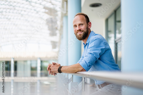 Confident businessman staning in office building leaning on railing photo