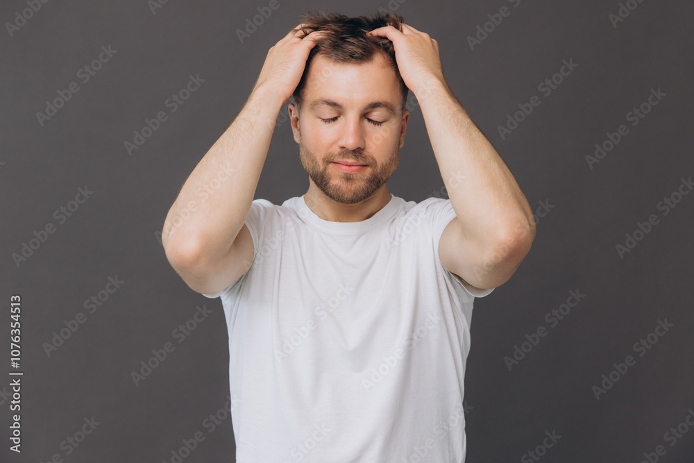Cute bearded man massaging his scalp on gray background in studio, beauty and care concept Cute bearded man massaging his scalp on gray background in studio, beauty and care concept