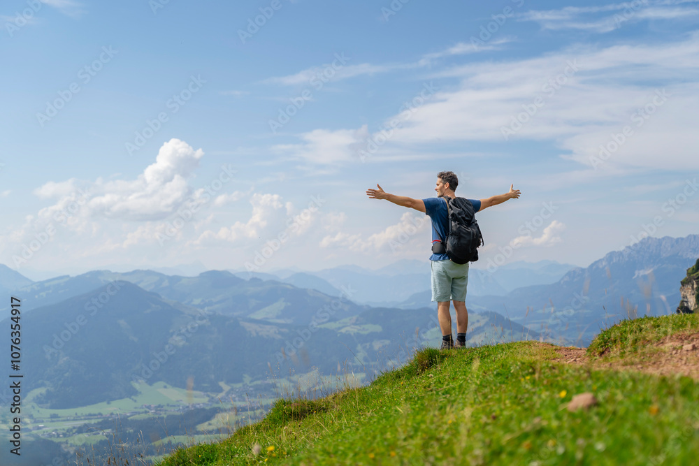 Carefree backpacker standing with arms outstretched under blue sky