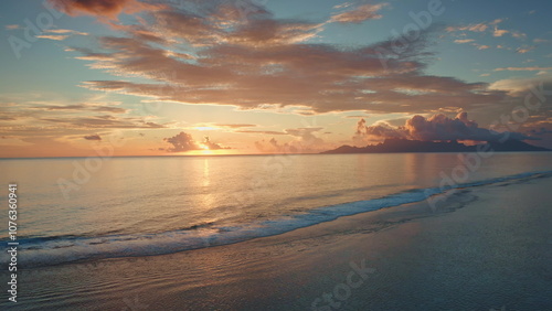 Golden sunset illuminate tranquil ocean, Moorea island in background, tropical paradise scene in French Polynesia. Colorful orange cloudy sky reflect in sea waves. Exotic summer travel. Aerial flight