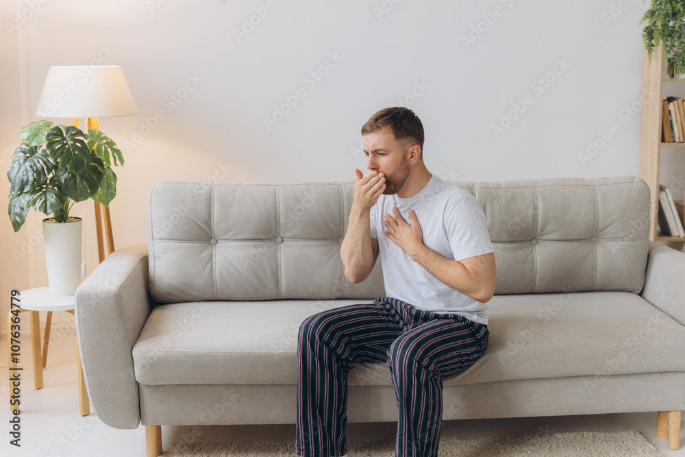 Sick man holding his chest in pain while coughing in the living room. Sore throat and cough, man with lung pain at home, health problems concept Sick man holding his chest in pain while coughing in the living room. Sore throat and cough, man with lung pain at home, health problems concept