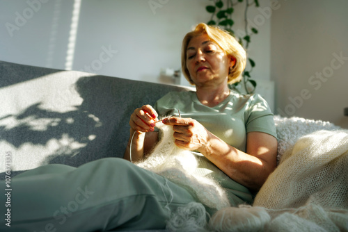 Senior woman knitting shawl and sitting on sofa at home photo