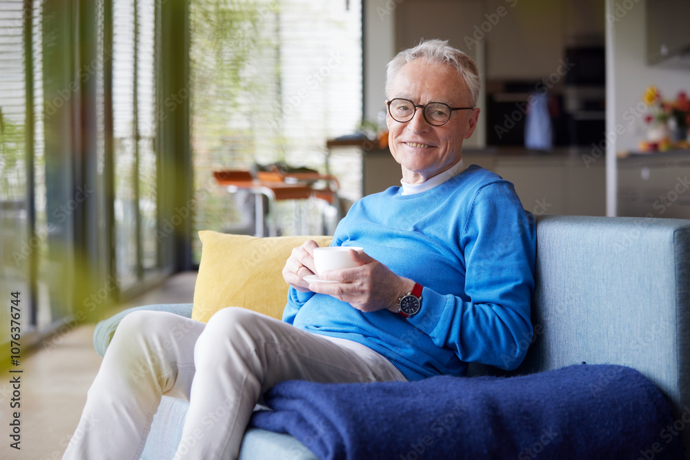 Senior man sitting on couch at home with cup of coffee Senior man sitting on couch at home with cup of coffee
