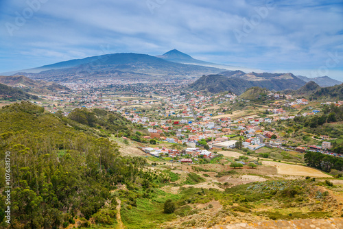 A scenic panorama of Tenerife with verdant hills, a town with mixed architecture, and the majestic Mount Teide rising in the background