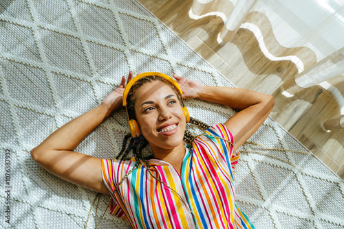 Smiling woman wearing wireless headphones and listening to music on carpet photo