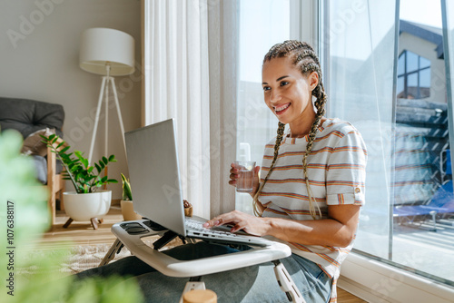 Happy freelancer holding glass of water and working on laptop at home photo