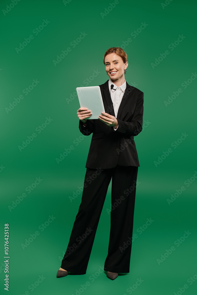 A stylish presenter in formal attire holding a tablet, set against green. A stylish presenter in formal attire holding a tablet, set against green.