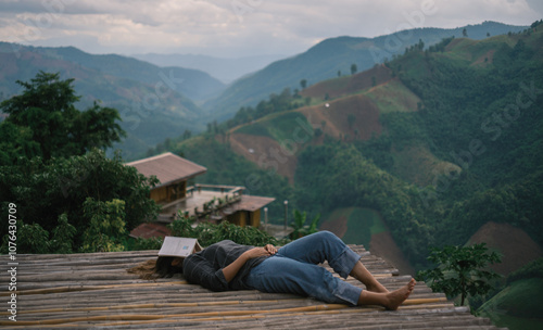 a woman lay down on a bamboo floor with a book on her face while travel in a mountain landscape