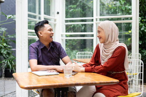 A joyful couple sharing laughter and bonding at an outdoor cafe table, surrounded by lush greenery and cozy atmosphere. Perfect representation of happiness and connection.