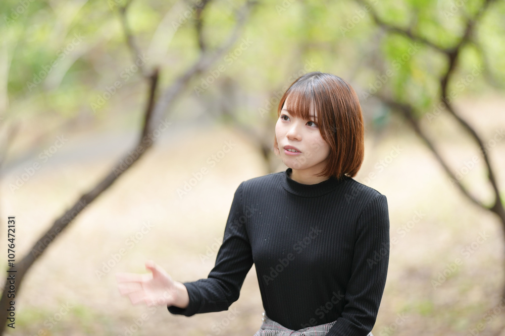 A young woman in her twenties with short hair wearing a black knitted long-sleeved shirt is sitting on a bench in the forest and explaining something. A young woman in her twenties with short hair wearing a black knitted long-sleeved shirt is sitting on a bench in the forest and explaining something.