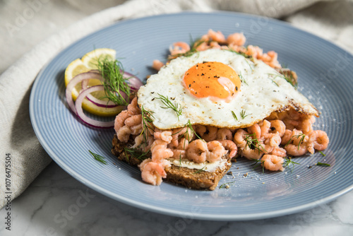Norddeutsche Friesisches Krabbenbrot mit  Nordseekrabben  Spiegelei, Brot, Butter, Zitrone, rote Zwiebel und Dill auf blau Porzellan Teller, Serviette und hell Marmor Hintergrund
