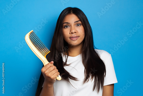 Girl in blue and white with comb on the . hair female w concept. girl with comb in her hands on a blue . a girl in blue stands with a comb in her hands lifestyle on a blue. photo