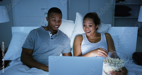 Shocked, couple and watching on laptop at night for horror movie, eating popcorn and bonding together. People, relaxing and snack with online streaming, scary film and entertainment services at house