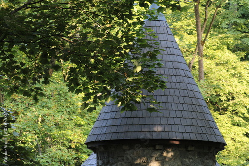 A serene view of a stone tower with a conical roof surrounded by lush green trees in a peaceful forest setting during daylight