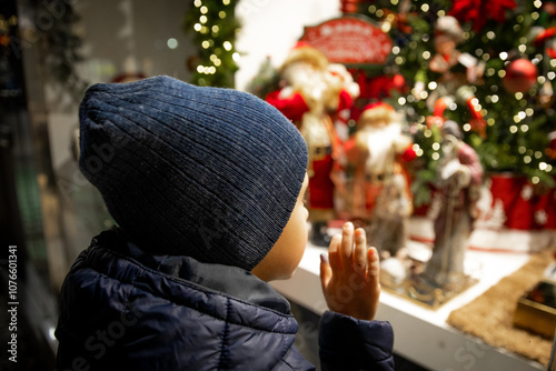 Child in evening in city looks at festive shop window with toys in a Christmas shop window.