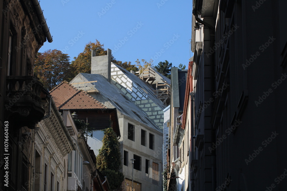 Fototapeta premium Modern architecture emerges among historic buildings under a clear sky in an urban setting during late afternoon