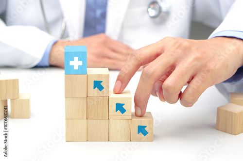 Two fingers of doctor is walking up stairs wooden blocks with medical symbol icons. Concept of Success, progress and growth.