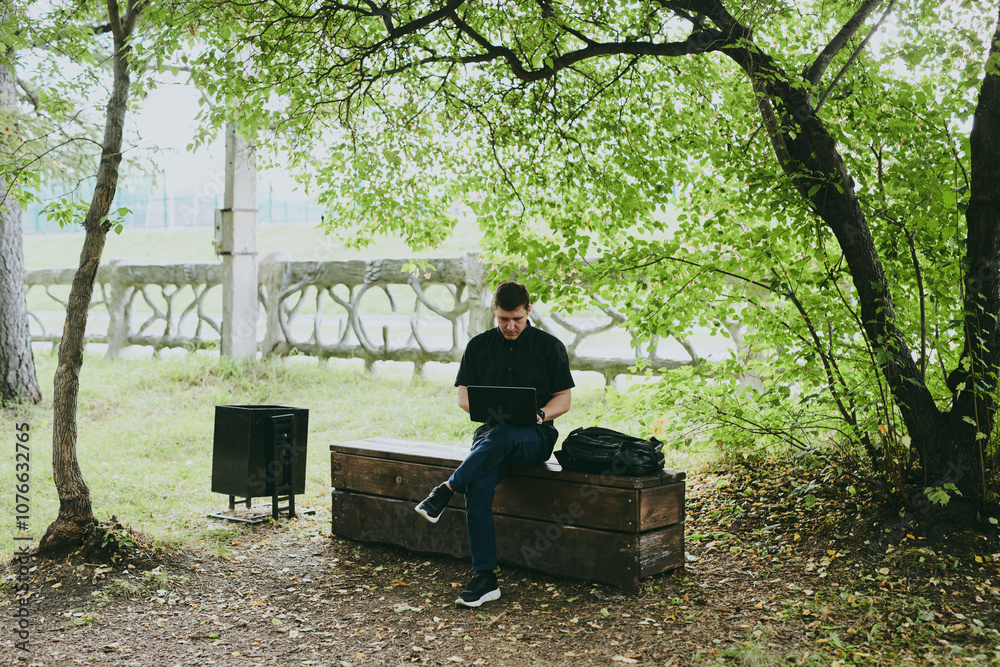 Fototapeta premium Portrait of young freelance programmer man working with laptop in forest park, software developer, IT technologies