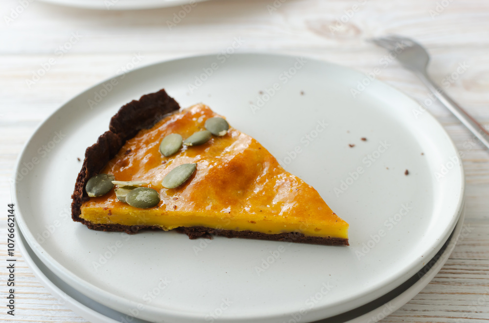 A piece of orange pumpkin pie with dried seeds on a white plate on the table. Autumn mood. Tea time concept. Horizontal orientation A piece of orange pumpkin pie with dried seeds on a white plate on the table. Autumn mood. Tea time concept. Horizontal orientation