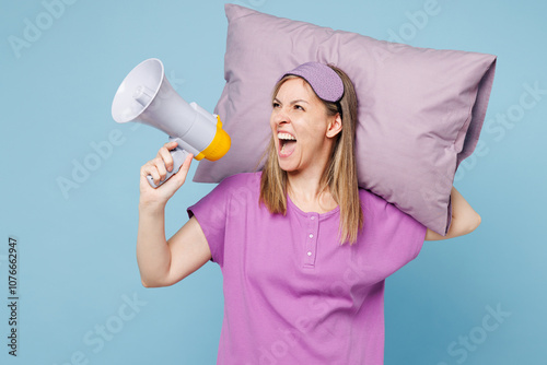 Mad sad indignant young woman wear purple pyjamas jam sleep eye mask rest relax at home hold pillow scream in megaphone isolated on plain pastel light blue cyan background. Bad mood night nap concept. photo