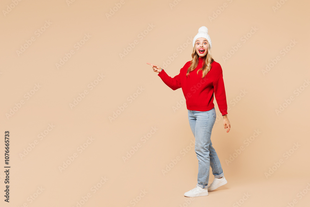 Full body side view merry young woman wear red warm sweater hat posing walking going point finger aside isolated on plain pastel beige background. Happy New Year celebration Christmas holiday concept. Full body side view merry young woman wear red warm sweater hat posing walking going point finger aside isolated on plain pastel beige background. Happy New Year celebration Christmas holiday concept.