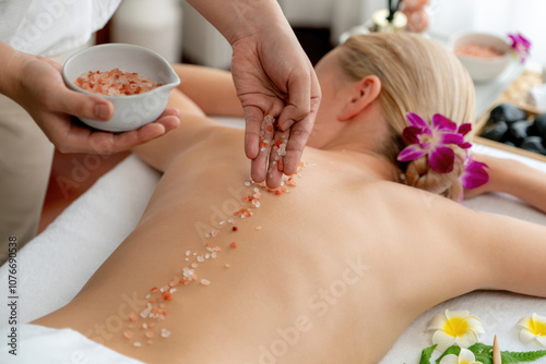 Woman customer having exfoliation treatment in luxury spa salon with warmth candle light ambient. Salt scrub beauty treatment in health spa body scrub. Quiescent