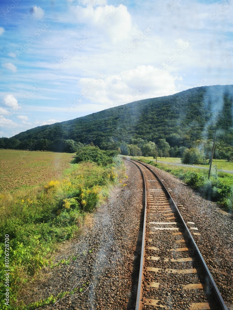 Scenic railway track winding through lush green fields and hills on a sunny day Scenic railway track winding through lush green fields and hills on a sunny day