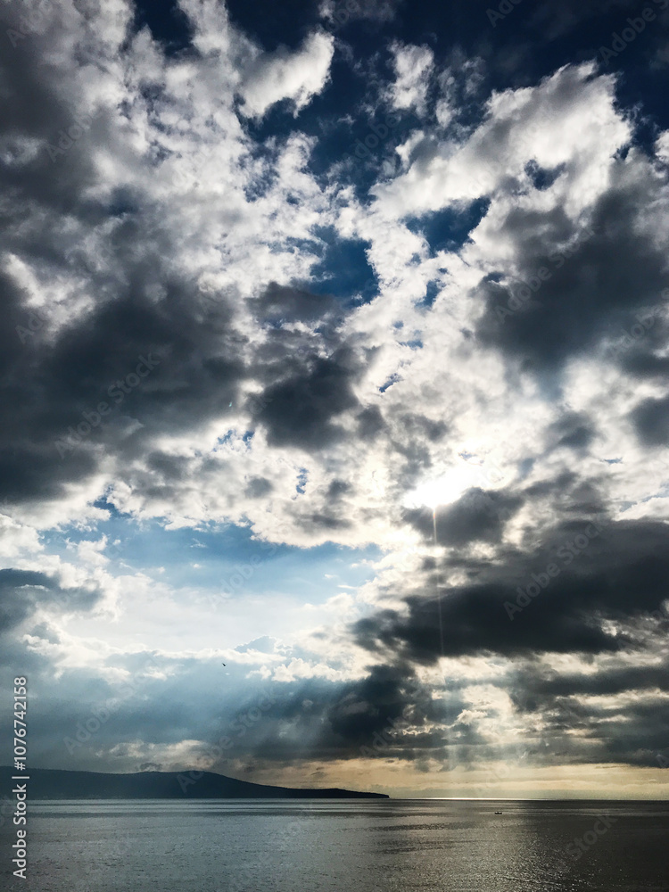 Dramatic cloudy sky over calm ocean with sunlight peeking through Dramatic cloudy sky over calm ocean with sunlight peeking through