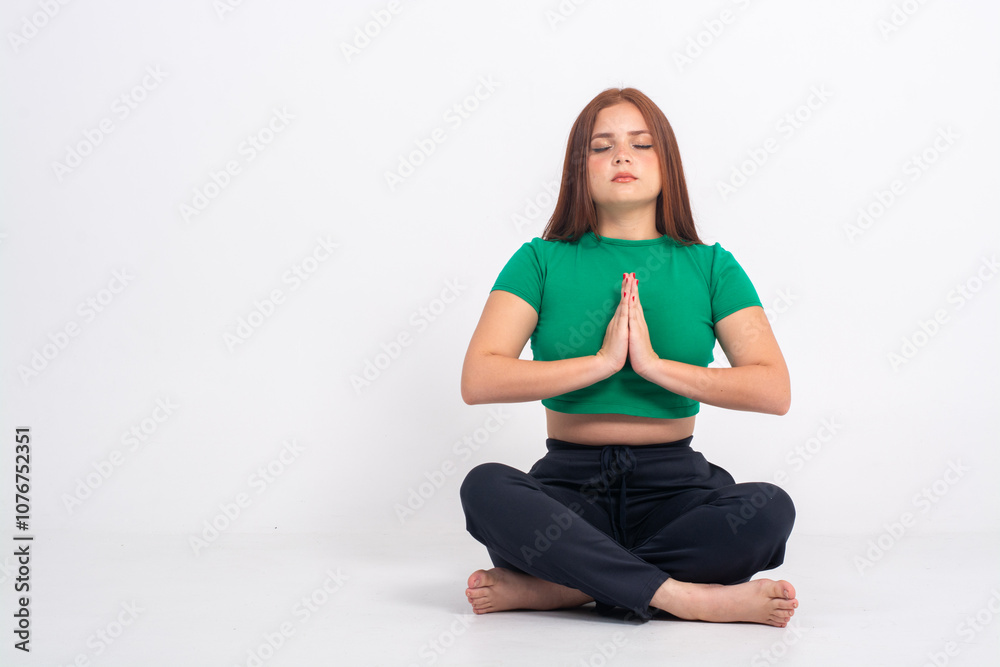 Yoga girl with palms together closed eyes and sitting on the ground taking deep breath meditation working on her wellness isolated on a white background Yoga girl with palms together closed eyes and sitting on the ground taking deep breath meditation working on her wellness isolated on a white background