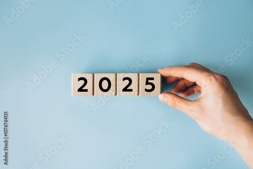 2025 New Year Loading. Female hand moving wooden blocks with Loading bar between 2024 and 2025 on a blue background. Concept for transition, progress, new year, and future plans