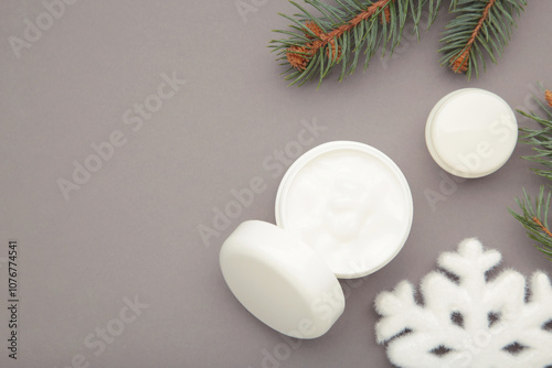 Cold protecting winter cream concept. Jar cosmetics with snowflakes and fir tree branches on grey background. Winter seasonal skin care photo