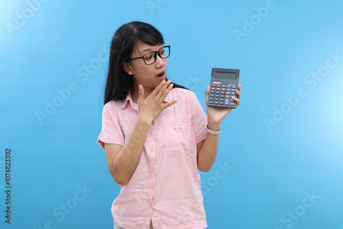 Young Asian woman feel amazing hold in hands calculator isolated on blue background studio portrait.