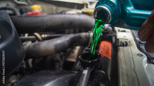 Closeup of changing the coolant of a car radiator in the engine bay of a pickup truck. Emerald green oil poured from a gallon.