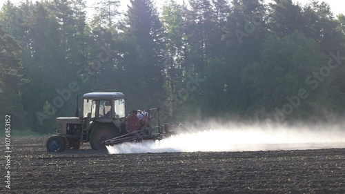 Farm tractor applies chemicals to potato crop by spraying from nozzles on boom.