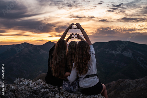 Tree happy female friends making heart shape with their hands with sunset in the background, sisters making a heart symbol in nature, friendship of young people, girl best friends at the sundown