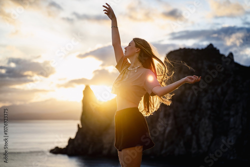 Canvas Print Young woman dancing at sunset on a summer day among sea and mountains background