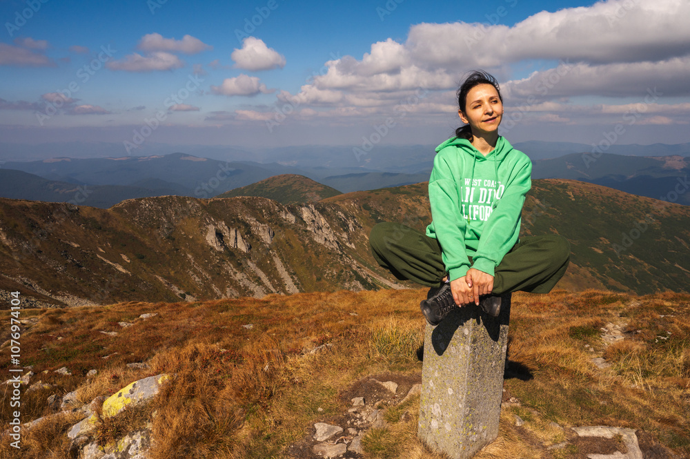 Obraz premium Woman sitting on a rock in the mountains, basking under the sun. Tranquil moment of solitude amidst stunning nature, perfect for wellness and travel themes 
