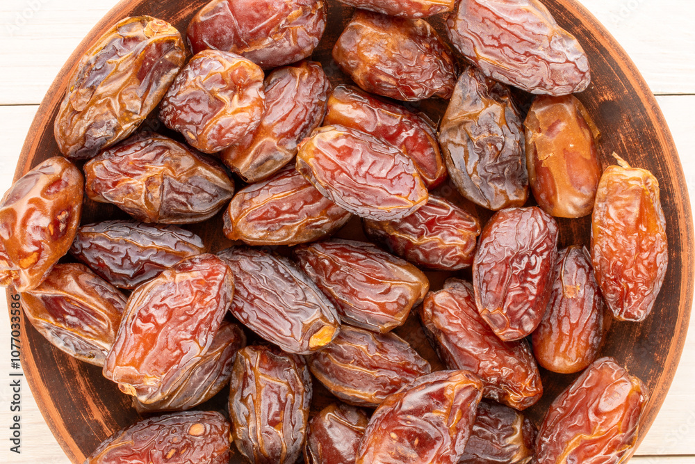 Obraz premium Several sweet dried pitted dates on a clay plate, macro, top view.