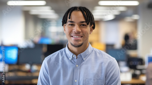 A young Black male professional smiling confidently in a bright office environment, showcasing a welcoming demeanor and modern workspace.